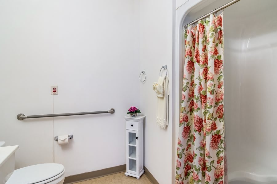 A clean bathroom with a floral shower curtain and small storage unit.