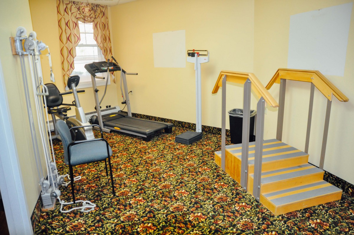 A small indoor fitness room with various exercise equipment including a treadmill, stationary bike, and weights.