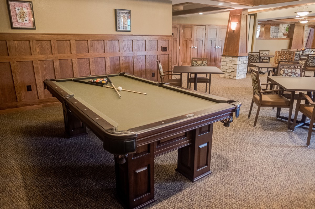 A spacious game room featuring a classic pool table with wooden detailing, surrounded by elegant wood paneling and seating areas.