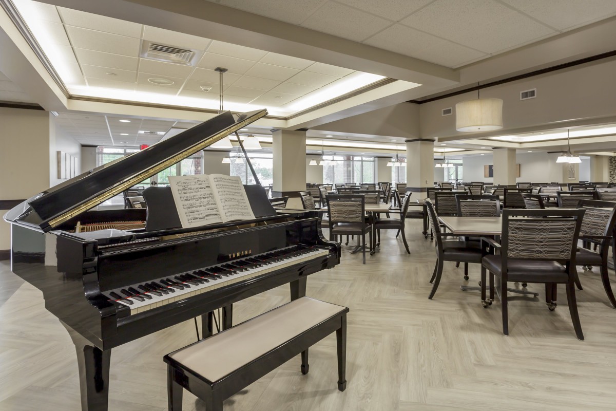 A grand piano in a spacious dining area with tables and chairs.