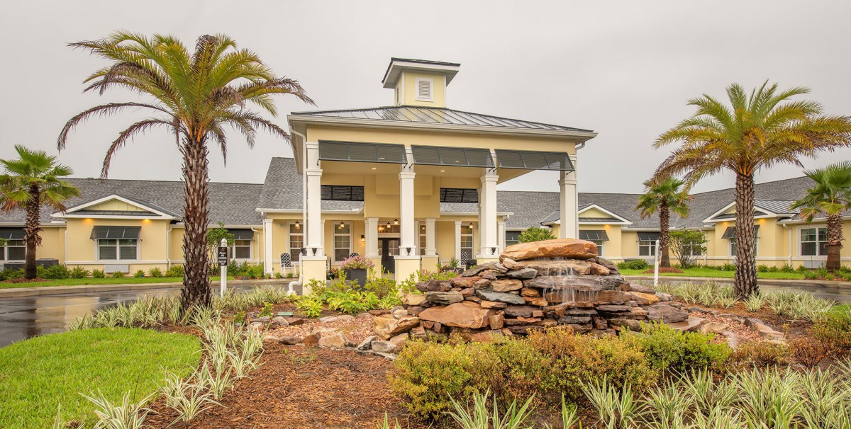 A grand entrance to a building with tall columns and a landscaped fountain.