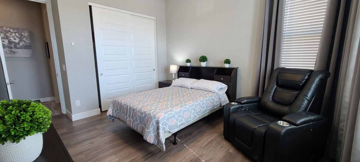 A cozy bedroom with a neatly made bed, nightstand, and decorative plants.