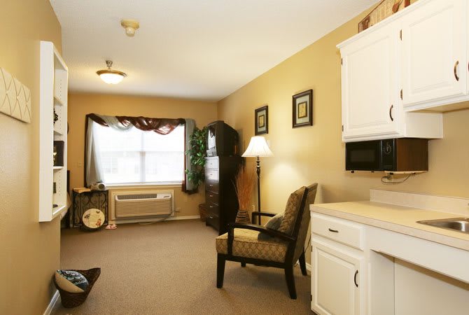 A cozy living room featuring an armchair, lamp, and decorative elements with a window letting in natural light.