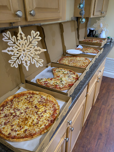 An array of pizzas displayed in their boxes, topped with various ingredients, set up in a cozy kitchen.