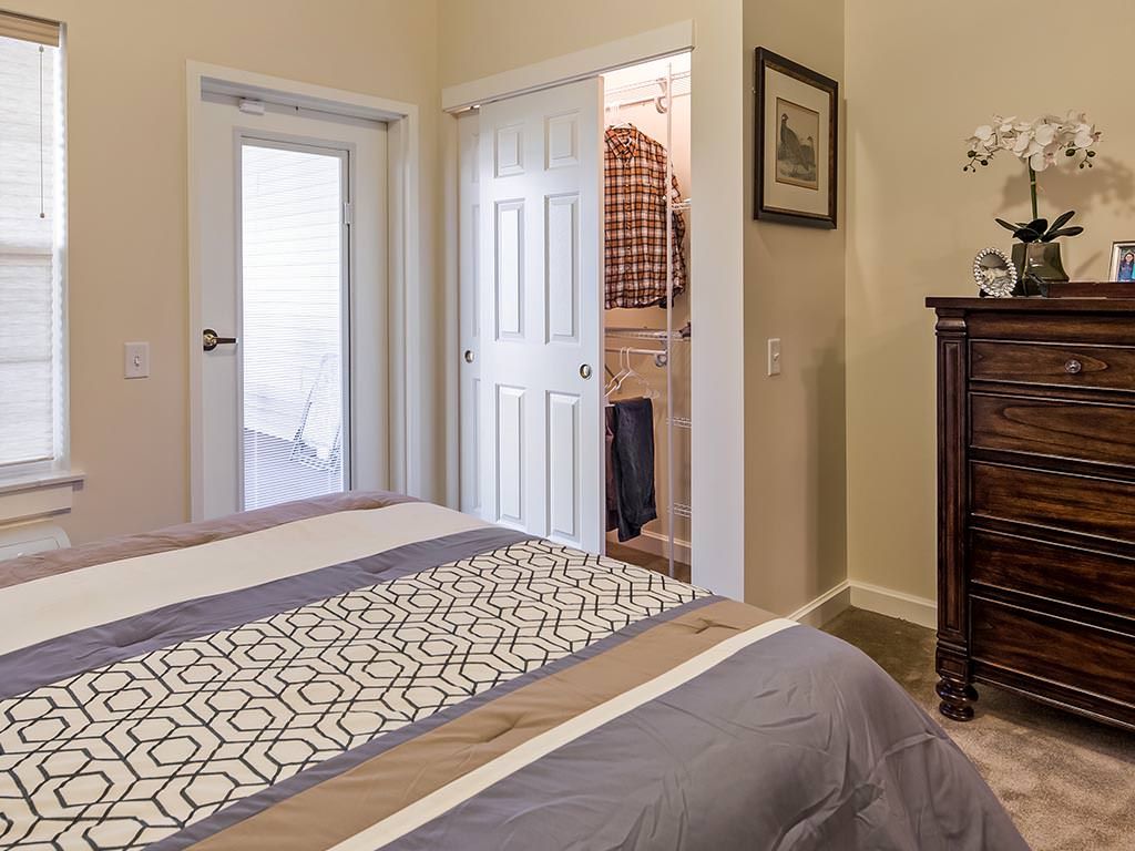 A cozy bedroom with a neatly made bed, an open closet, and a dresser.