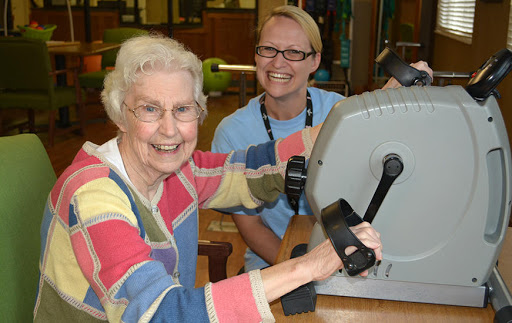 A joyful senior woman participates in a fitness session, supported by a staff member.