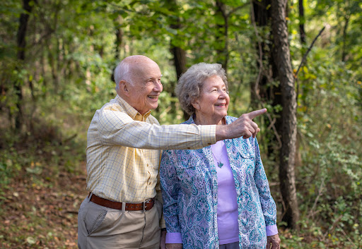 A joyful elderly couple enjoying a walk in the woods, pointing at something interesting.