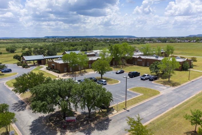 An aerial view of a school surrounded by trees and a parking lot in a rural setting.