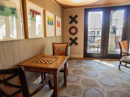 A cozy room with a chessboard table, decorated with colorful artwork and sunlight streaming through the doors.