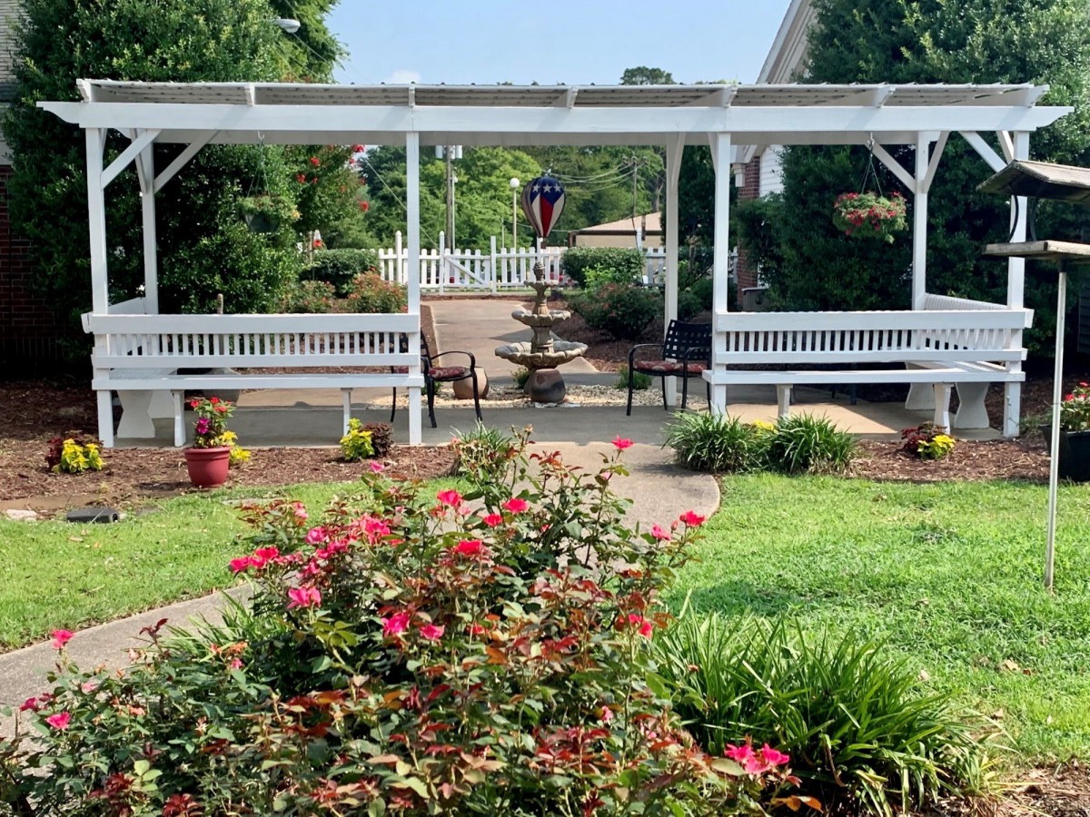 A beautifully landscaped garden with vibrant flowers, a pergola, and benches along a pathway.