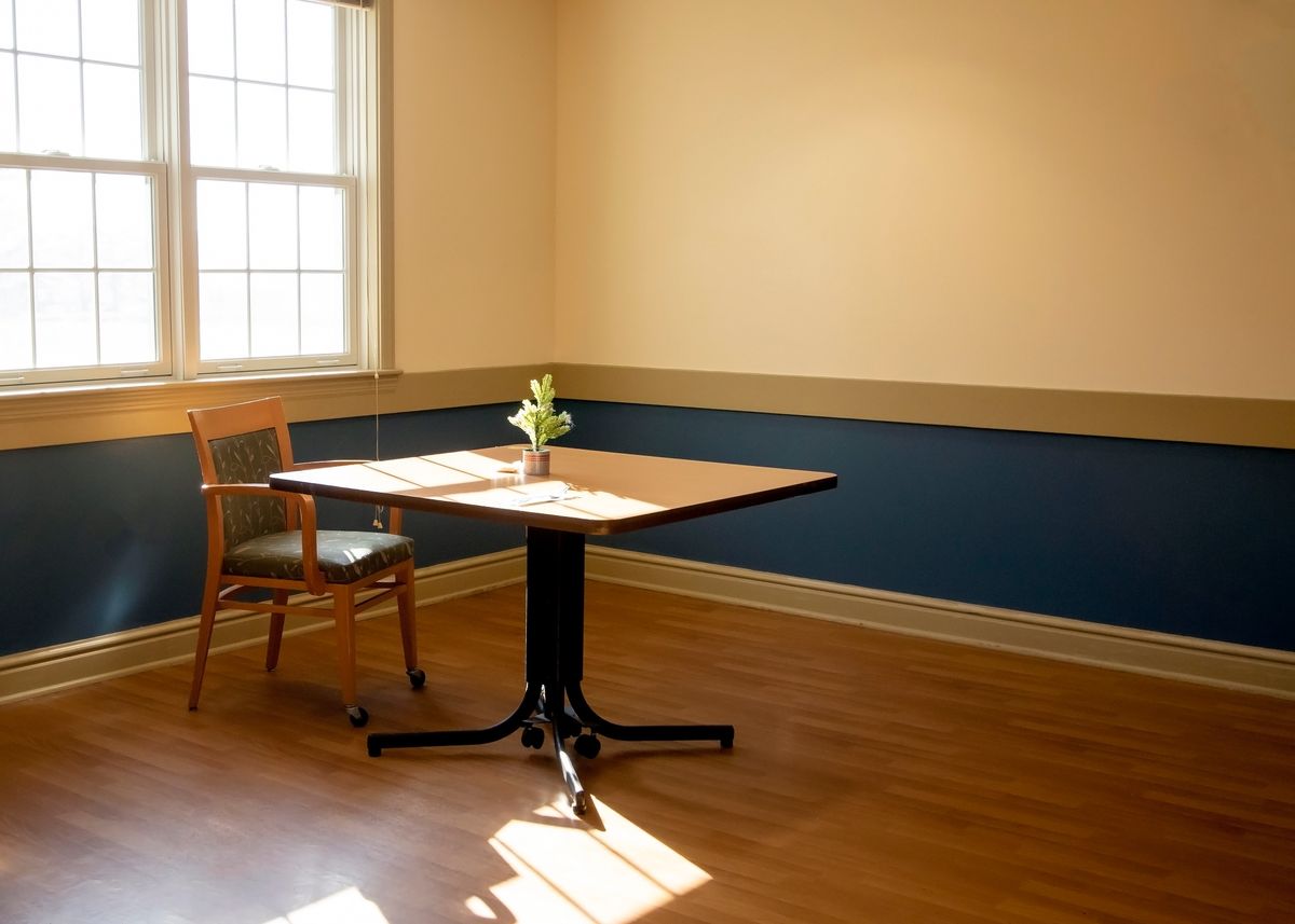 A minimalist room with a single table and chair near a window, accented by natural light and a small flower vase.