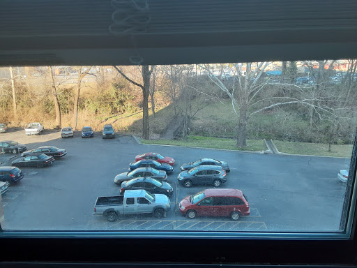 A view of a parking lot with several cars parked and trees in the background.