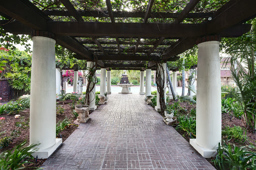 A serene garden pathway framed by columns and a trellis, inviting visitors to explore.