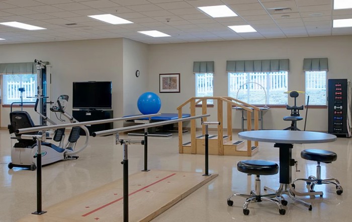A spacious rehabilitation room equipped with parallel bars, exercise ball, and various therapy equipment.