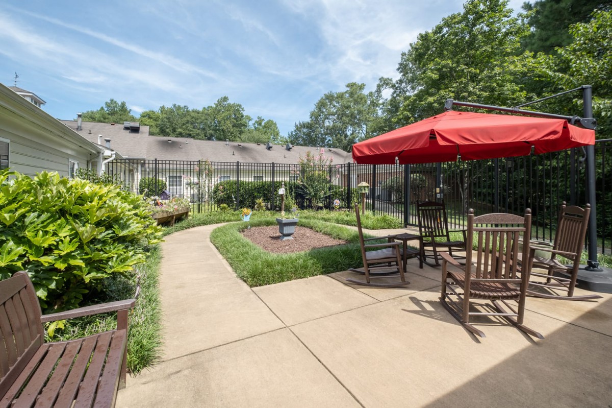 A peaceful garden with a pathway, outdoor seating, and a fountain under an open sky.