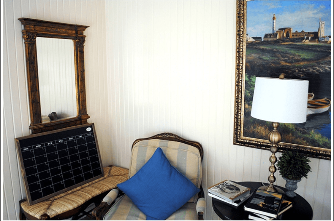 A cozy corner with a chair, mirror, and table lamp.