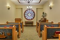 Interior view of a small chapel with wooden benches and a stained glass window.