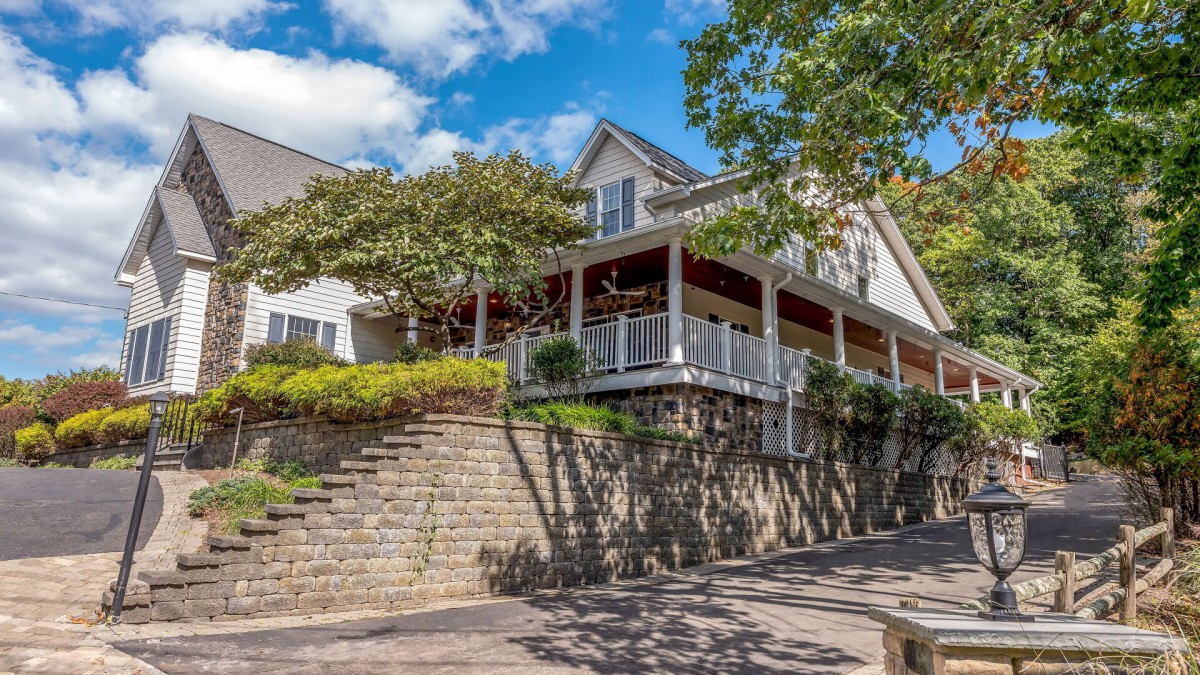 A charming residential house with a wraparound porch and stone landscaping.