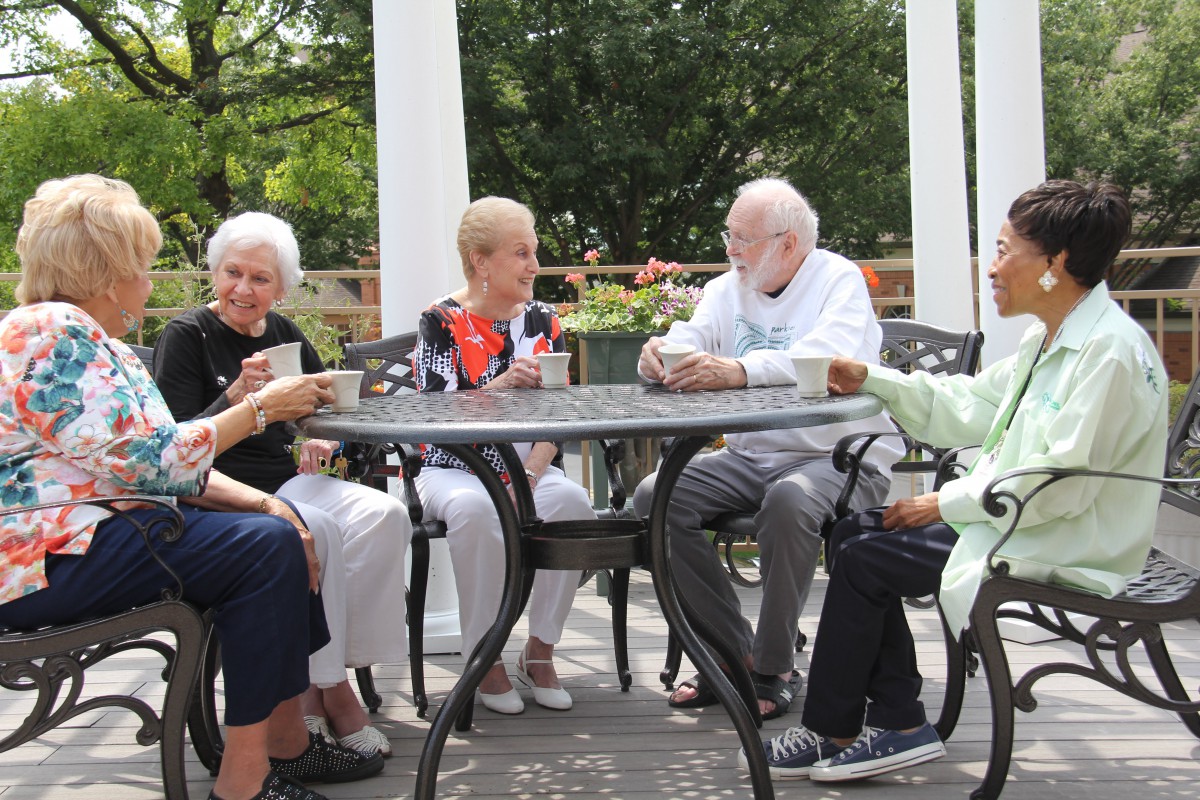 A group of seniors enjoying coffee and conversation on a patio.