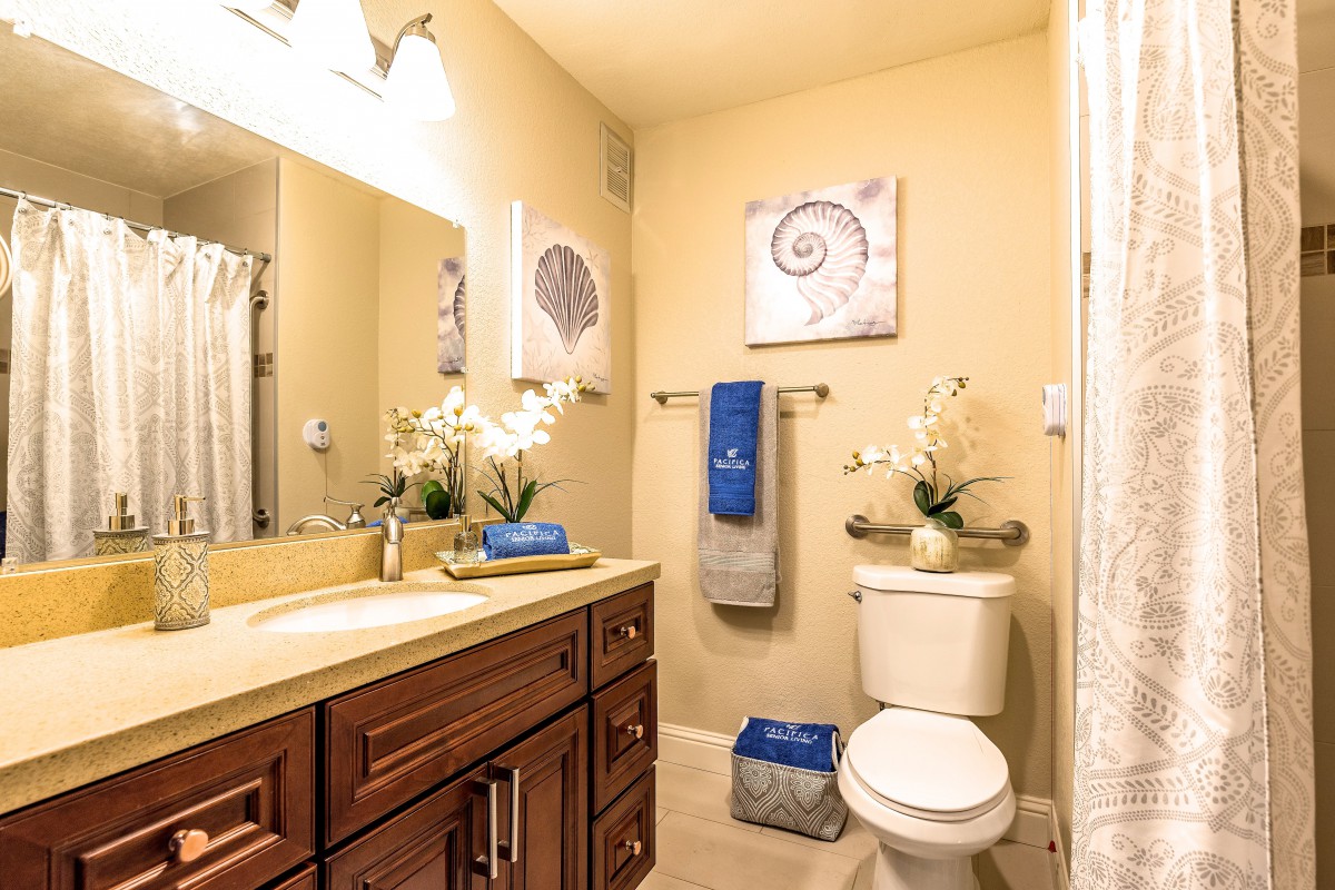 A well-decorated bathroom with elegant wooden cabinets, blue and gray towels, potted flowers, and seashell-themed artwork.