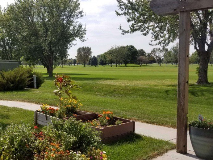 A serene park scene with a manicured lawn, vibrant flowers in raised beds, and trees under a partly cloudy sky.