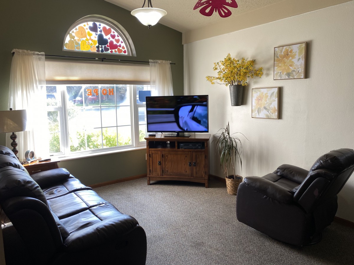 A cozy living room with a television, comfortable seating, and large windows allowing plenty of natural light.