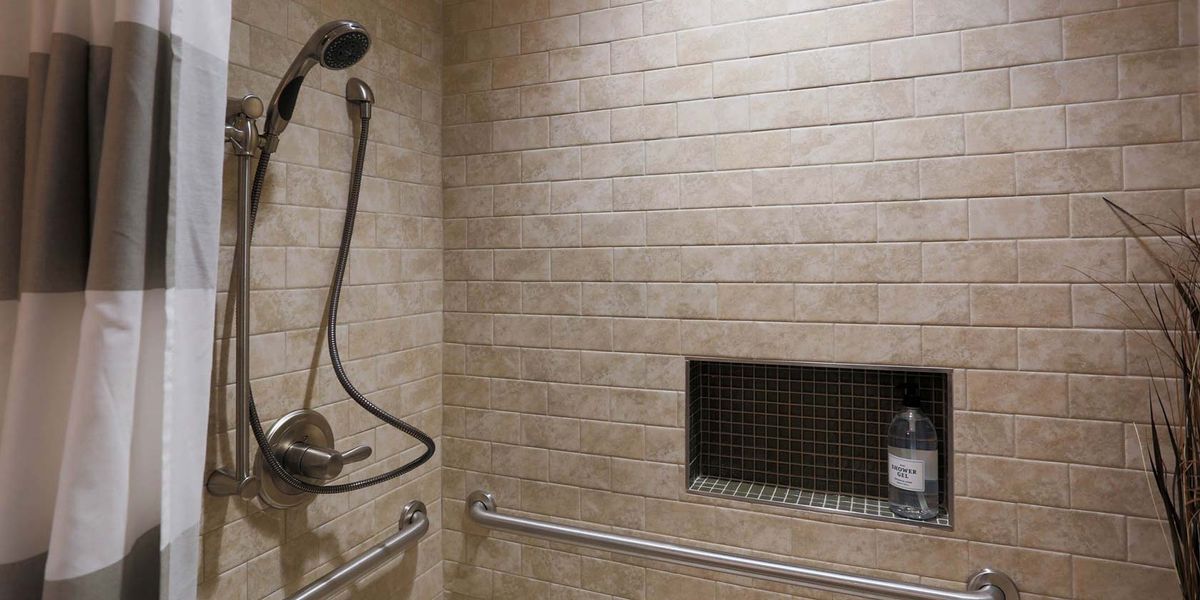 A modern bathroom shower with tiled walls, a handheld showerhead, grab bars, and a built-in wall niche.