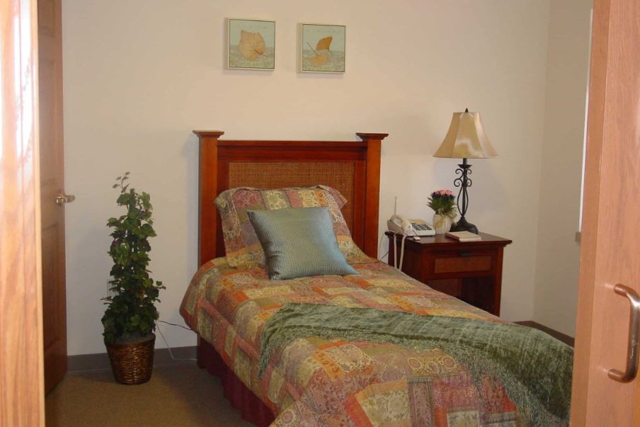 A cozy bedroom featuring a single bed with colorful bedding, a nightstand with a lamp, and wall art above the headboard.
