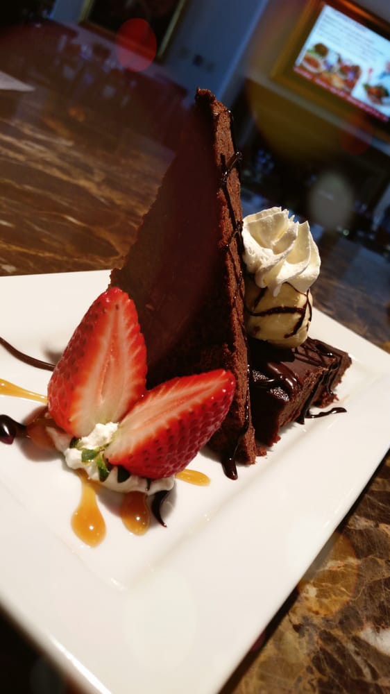A decadent chocolate cake slice garnished with fresh strawberries and whipped cream.