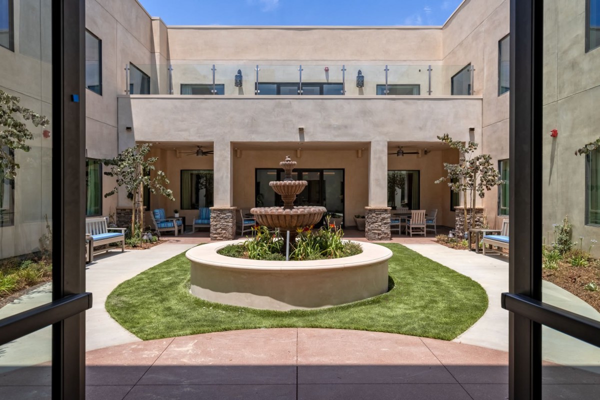A courtyard featuring a central fountain surrounded by a neatly maintained lawn and modern architecture.