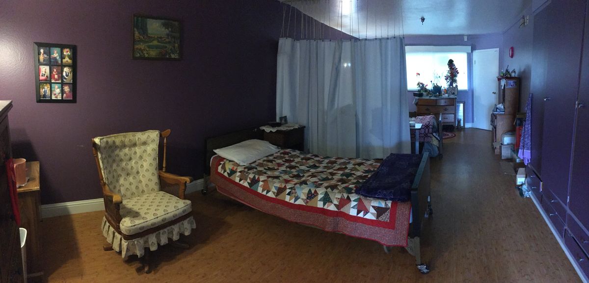 A cozy bedroom with a quilted bed, chair, and curtains.