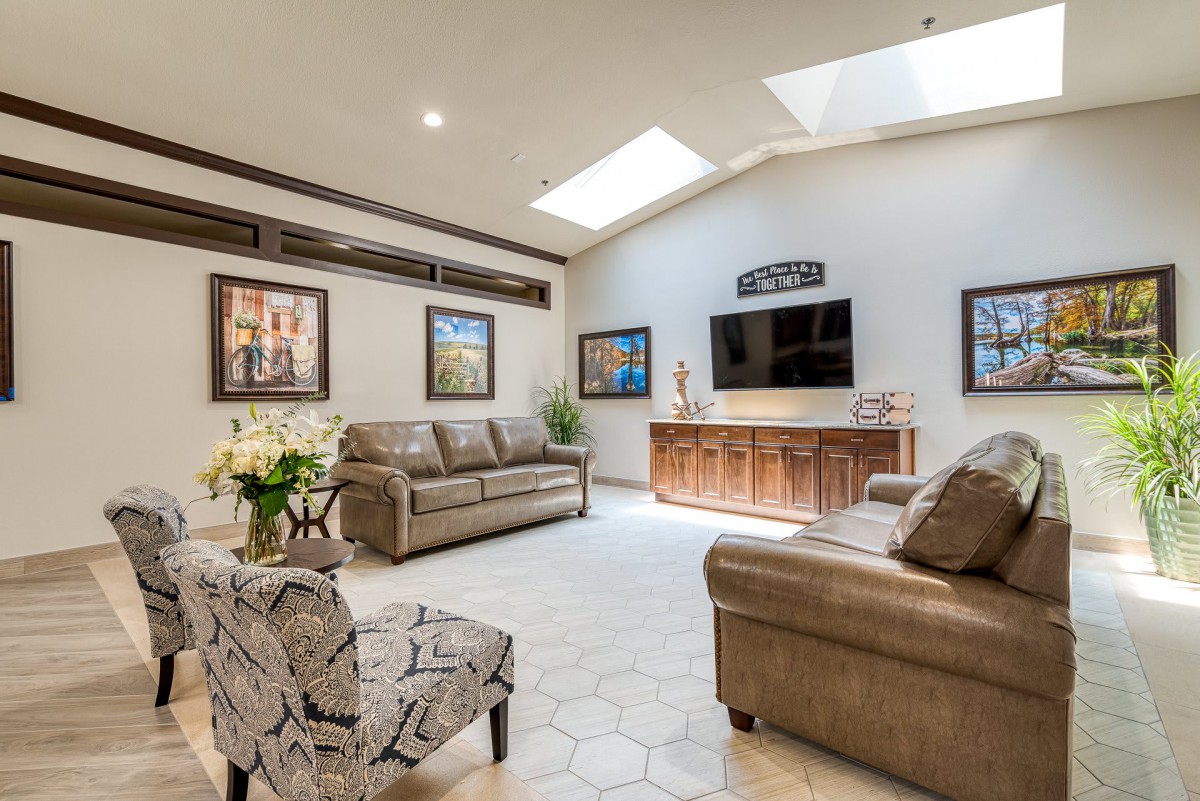 A spacious living room featuring comfortable seating, a television, artwork on the walls, and natural light from skylights.