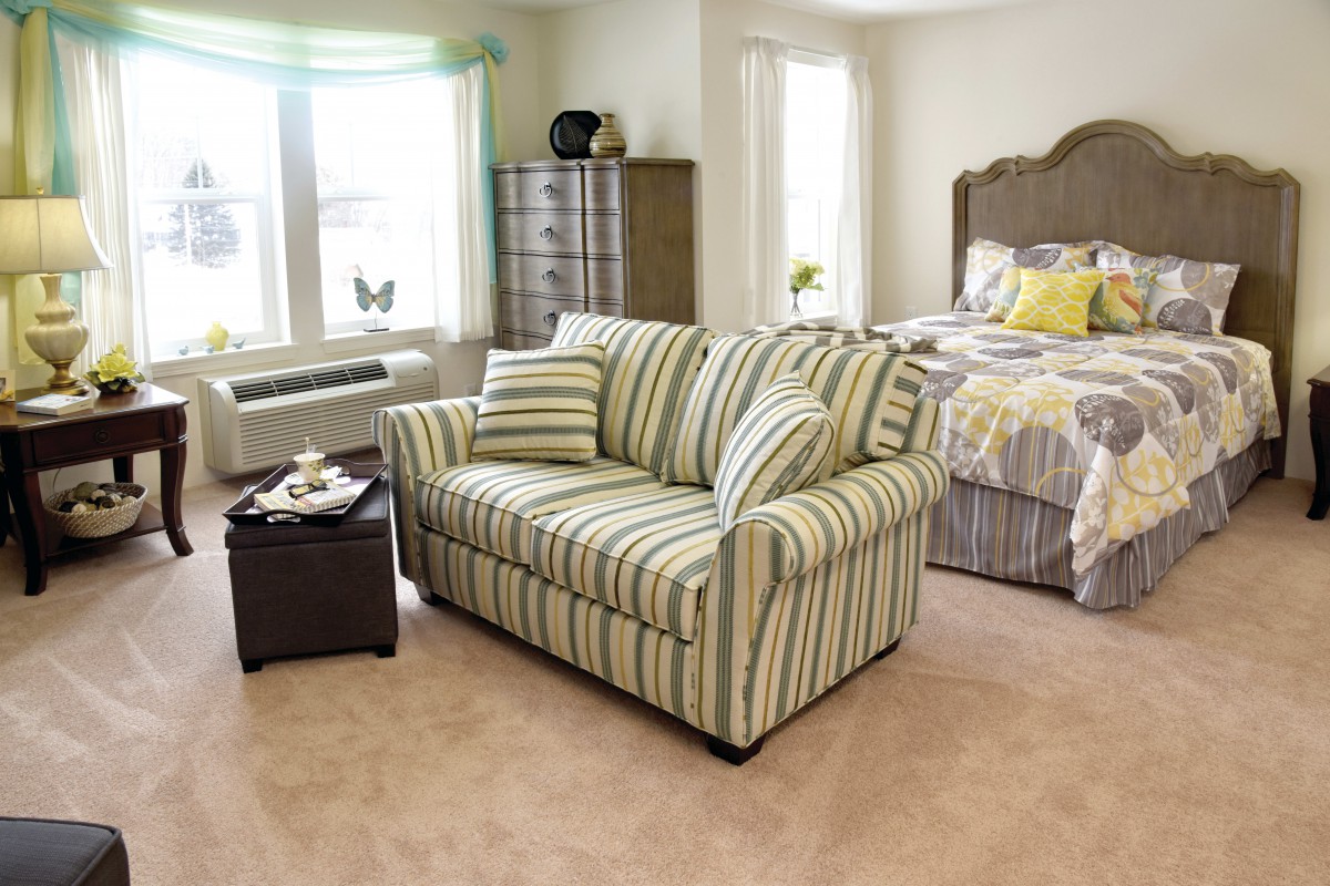 A cozy bedroom featuring a striped sofa, a large bed, and ample natural light from the windows.