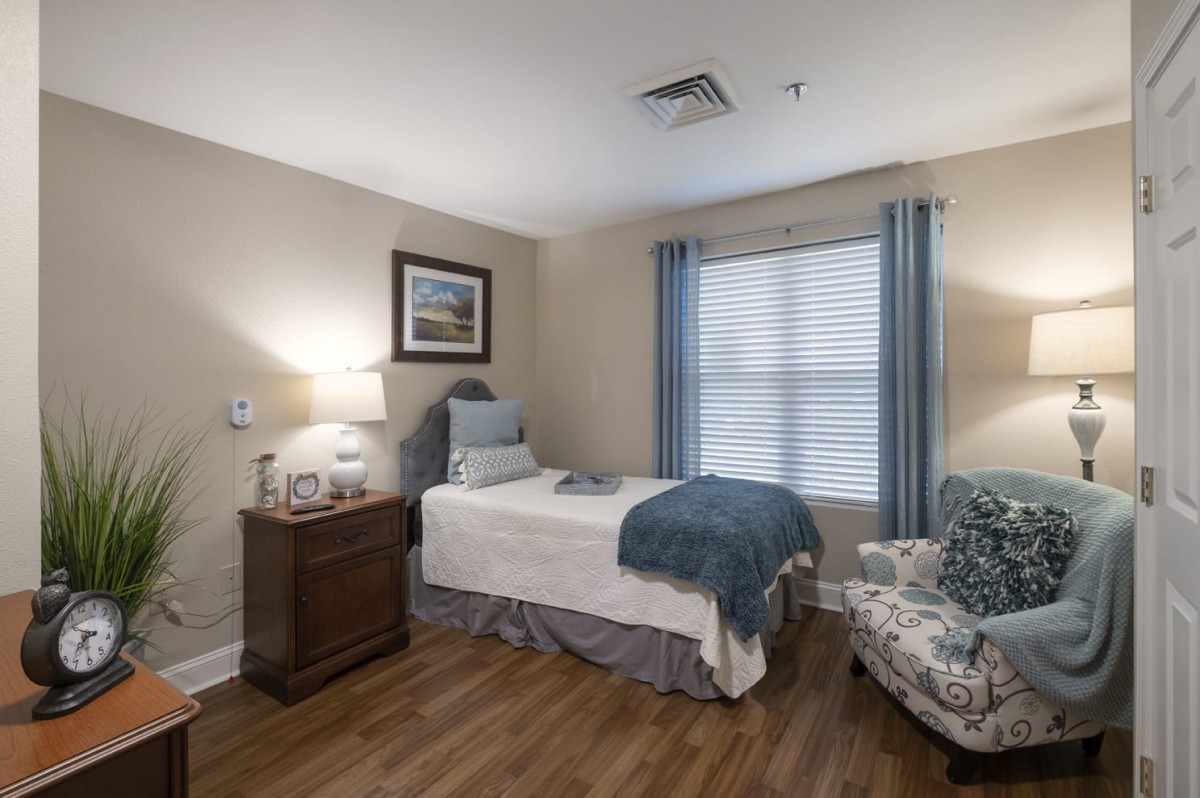 A cozy bedroom with a single bed, bedside table, and an armchair by the window.