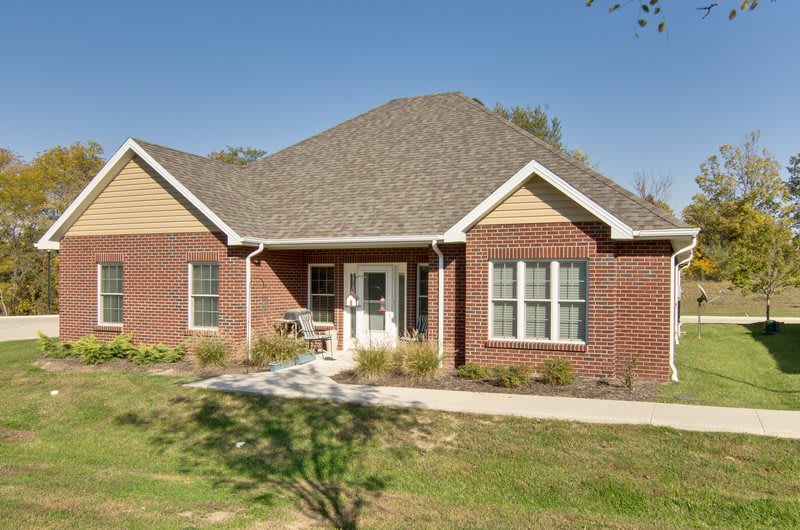 A brick residential house with a front yard and peaked roof.