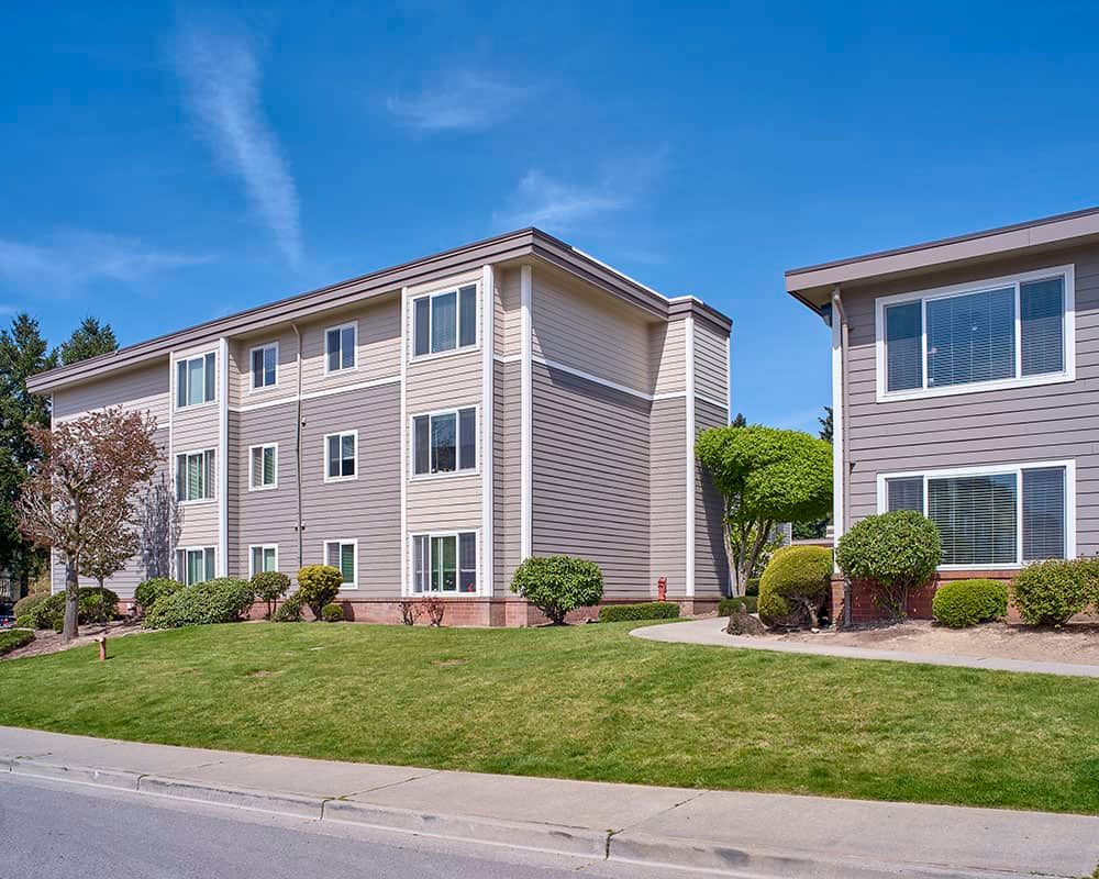 A residential apartment building with well-maintained landscaping under a clear blue sky.