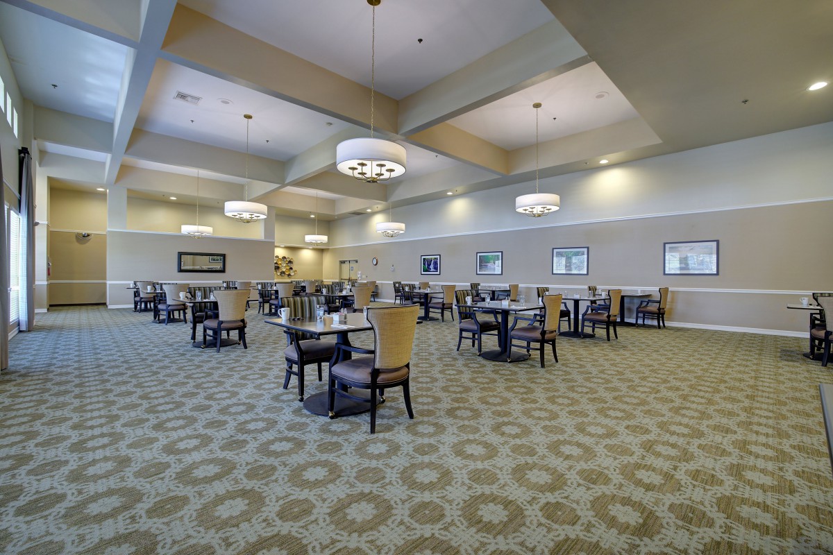 A spacious dining room with elegant chandeliers, arranged seating, and patterned carpeting.