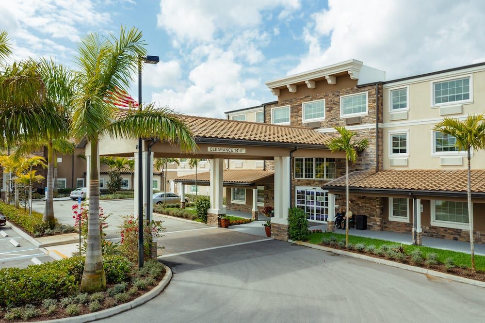 A hotel entrance with palm trees lining the driveway under a partly cloudy sky.