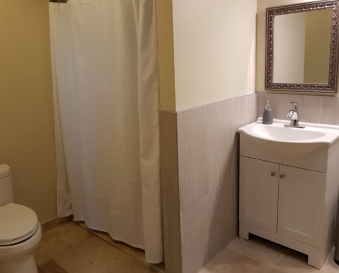 A bathroom featuring a shower with a curtain, a sink with a vanity and mirror, and a toilet.