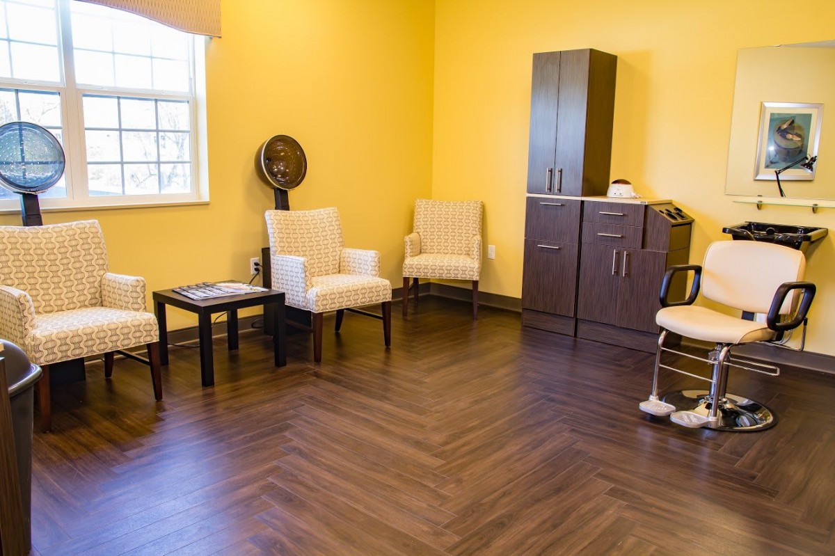 A cozy salon waiting area with chairs and a hair dryer against a bright yellow wall.