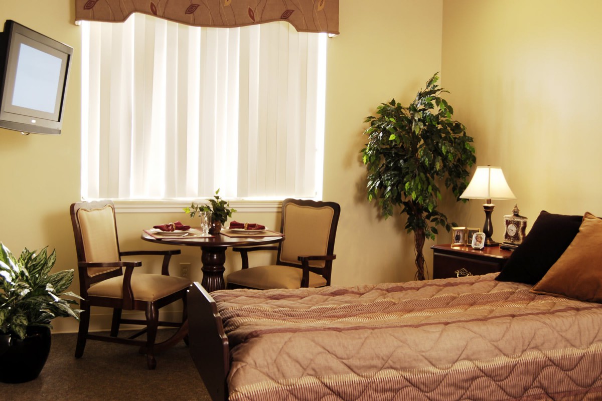 A cozy bedroom with a comfortable bed, a small dining table with chairs, and a lamp on the nightstand.