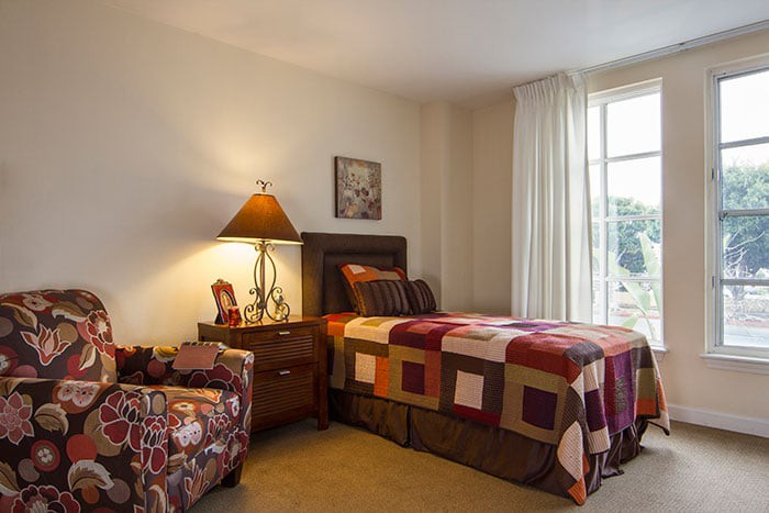 A cozy bedroom with a single bed, nightstand, and window with curtains.