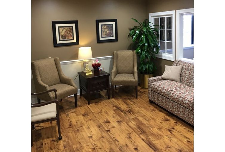 A cozy living room featuring a sofa, two chairs, a lamp on a side table, and decorative artwork on the walls.
