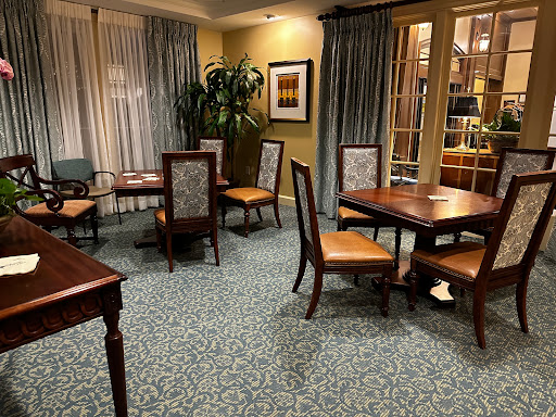 A cozy dining area featuring wooden tables and chairs with a green carpet and soft lighting.
