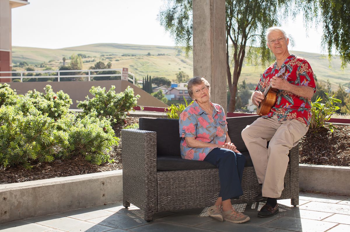 An elderly couple enjoying a sunny day on the patio, with one playing guitar.