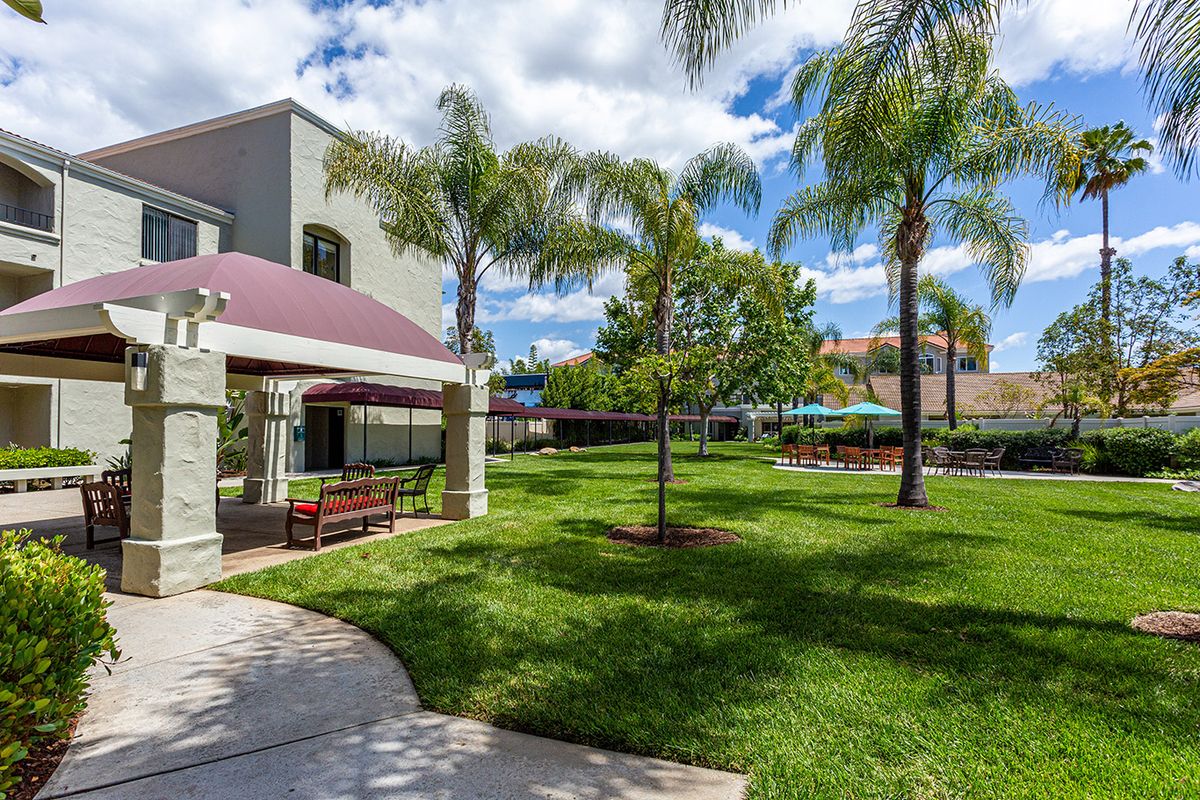 A well-maintained garden with palm trees and a building under a partly cloudy sky.