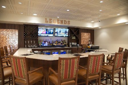 A modern bar area with a marble countertop, wooden chairs, and multiple television screens.