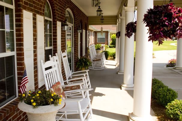 A cozy porch with white rocking chairs and hanging plants.
