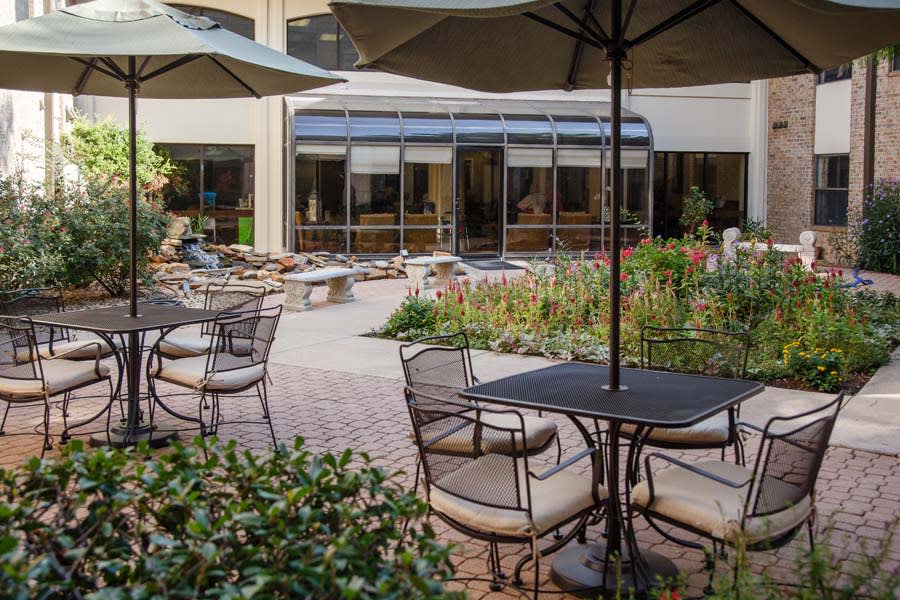 An inviting outdoor patio area with tables, chairs, and umbrellas overlooking a lush garden setting.