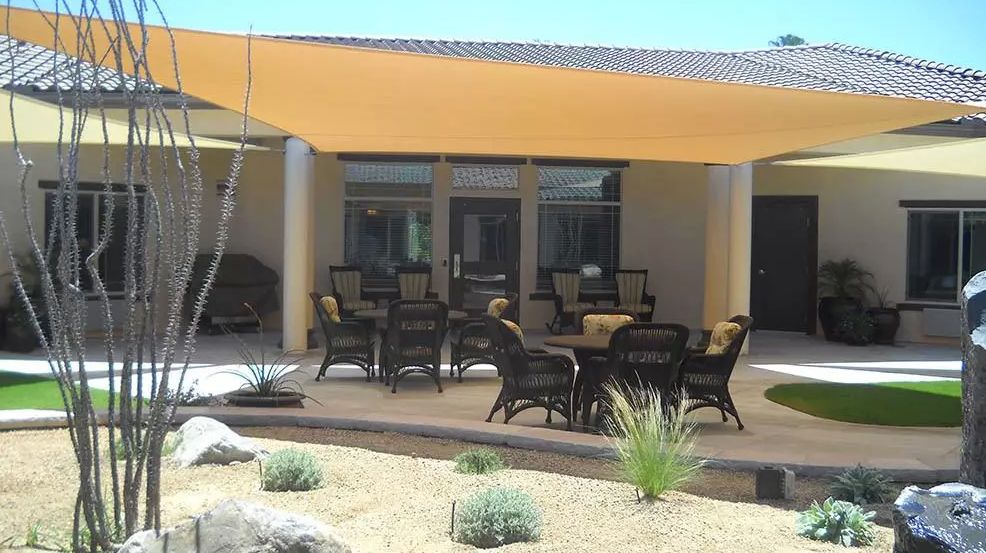 A cozy patio with outdoor seating and a shade sail, set against desert landscaping.